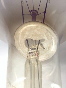 Pie y deflector térmico construido en metal, sostenido por una lámina metálica soldada a uno de los alambres de acometida.
